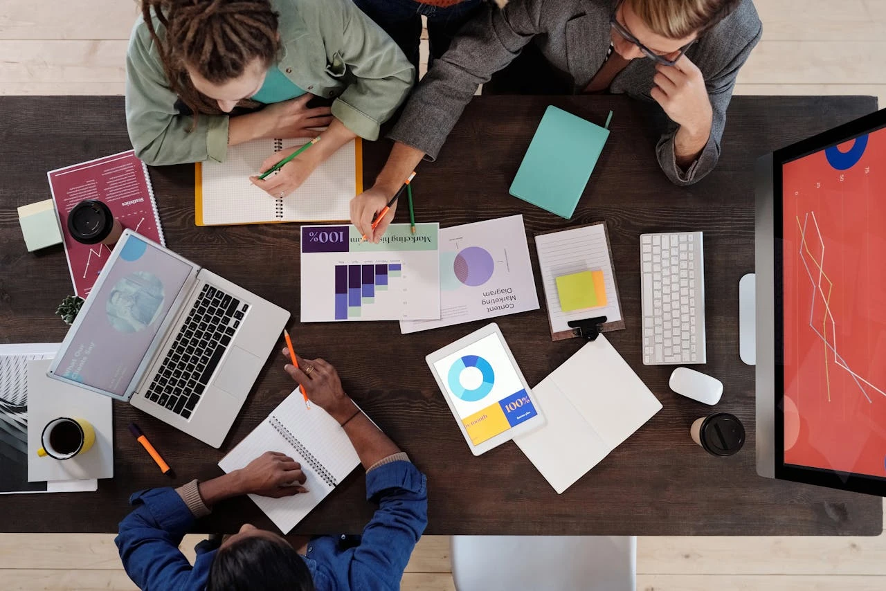A diverse group of professionals discussing investment strategies around a table with a laptop displaying stock market charts.